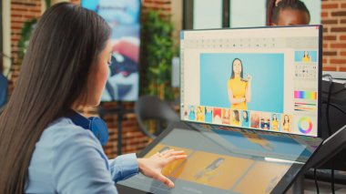 Kadın renkli editör tabletle rötuş yazılımı kullanıyor, ajans ofisinde multimedya üretimi üzerinde çalışıyor. Dokunmatik ekran ve stil ile fotoğraf ve resimleri düzenleyen Asyalı işçi.