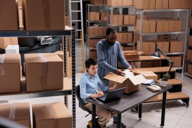 Çeşitli depo çalışanları teslimata hazırlanmak için müşteri siparişlerini paket halinde baloncuklu ambalaja koyuyorlar. Yönetici, depoda çalışırken nakliye bölümlerini yöneticisiyle tartışıyor.