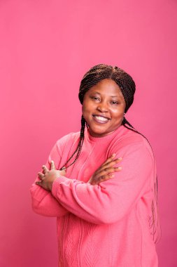 Dost canlısı genç yetişkin portresi stüdyoda pembe arka planda poz verirken kesişti, çekim sırasında kameraya gülüyordu. Neşeli yüzlü neşeli kadın eğleniyor, özgürce eğleniyor.