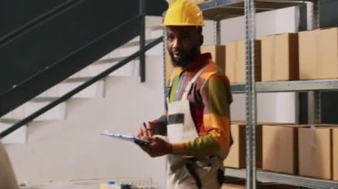 Kadın yönetici depoda teslimat kağıtlarını imzalıyor, ürün siparişini hazırlamak için envanter listesini gözden geçiriyor. Çeşitli meslektaşlar depodaki sevkiyat lojistiğini kontrol ediyor. El kamerasıyla..