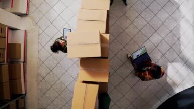 Depoda çalışan iki kişi, paketleri dizüstü bilgisayar ve tabletle kontrol ediyor. Perakende mağaza teslimatı için çeşitli depo yöneticileri teftiş planlıyor. İHA atışı. Hava görünümü.
