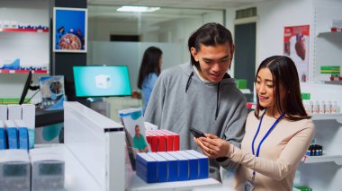 Woman specialist looking at smartphone to give pills to client, searching for medical treatment on shelves. Showing drugs and pharmaceutical products, pharmacy healthcare medicaments.