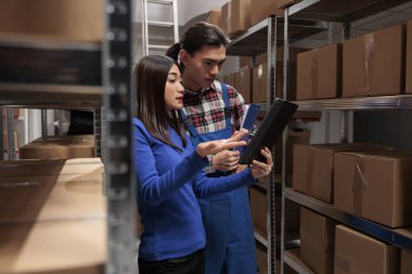 Depo çalışanları depo koridorunda dikilirken envanter kontrolü yapıyorlar. Depo Asyalı erkek ve kadın operatörler dijital tablet üzerindeki kalite yönetim raporunu analiz ediyorlar