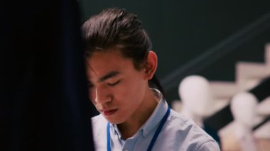 Asyalı çalışan, alışveriş merkezindeki müşteriler için şık ürünler ve aksesuarlar açmak, düzenlemek için mağaza hazırlıyor. Müdür yeni moda koleksiyonuyla askıları kontrol ediyor.
