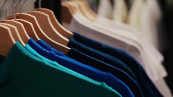 ファッショナブルな服で基本的なシャツ 空の現代的なブティックでいっぱいのハンガーやラックの選択的な焦点 ショッピングセンターは 顧客を待っている新しいファッションコレクションを装備 — ストック動画