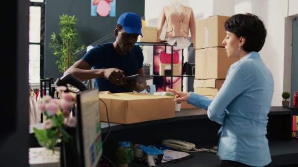 在让商店经理签署送货报告之前 非裔美国人快递员使用平板电脑对纸盒拍照 员工准备在现代精品店装运的套件 — 图库视频影像