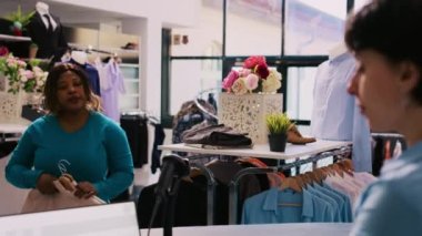 Modern butikte dükkan tarayıcısı kullanarak müşterileri tarayan beyaz işçi. Afro-Amerikalı bir kadın alışveriş merkezinden şık ürünler alıyor, yeni kıyafetler istiyor. Moda konsepti
