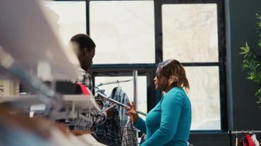 Modern butikte şık giyinen şık bir çift, gömlek kumaşlarını kontrol ediyor. Afrika kökenli Amerikalı müşteriler yeni moda koleksiyonu için alışveriş yapıyorlar, zarif ürünler ve aksesuarlar alıyorlar.