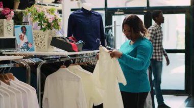 Afro-amerikan müşteriler şık gömlekleri inceliyor, giyim mağazasında günlük giyim kuşamlarıyla askılar tutuyor. Moda ürünleri ve aksesuarlar için alışveriş yapan şık bir kadın, indirimli kıyafetler alıyor.