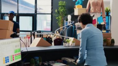 Mağaza çalışanı dağıtım raporunu imzalamak için kurye koyuyor, modern butikte teslimat detaylarını tartışıyor. Afro-Amerikan kurye alışveriş merkezine karton kutular getiriyor. Moda konsepti