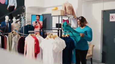 Asyalı bir çalışan, kadının şık kıyafetler almasına yardım ediyor, giysi mağazasında gömlek malzemelerini tartışıyor. Afro-amerikan müşteri yeni moda koleksiyonuna bakıyor.