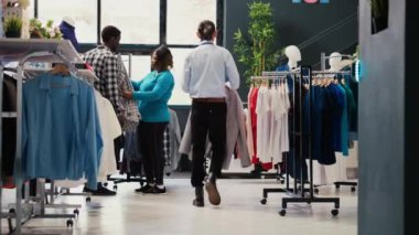 Zarif gömlek almak için alışveriş yapan şık bir çift modern butikten almadan önce kıyafet malzemelerini analiz ediyor. Giyim mağazasında yeni moda koleksiyonu olan şık müşteriler askılara bakıyor.