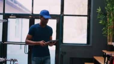 Afro-Amerikan kurye elinde bir tablet bilgisayarla mağaza müdürüne gidip müşterilerin detaylarını modern butikte tartışır. Çalışan alışveriş merkezinde teslimat için paketler hazırlıyor
