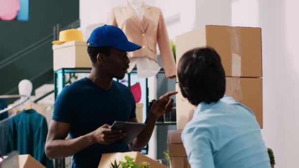商店员工签署运输报告 在购物中心与非洲裔美国信使讨论物流问题 时尚经理为顾客准备在现代精品店交货的套件 — 图库视频影像