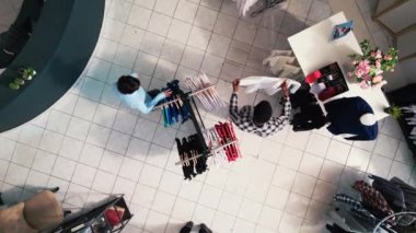 İnsansız hava aracı, modern butikte yeni moda koleksiyonlarıyla dolu askılara bakarak, çeşitli müşterilerin şık kıyafetler satın alışlarını görüntüledi. Müşteriler giyim mağazasından moda ürünler alıyorlar