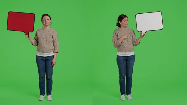 Stock image Smiling happy girl holding carton speech bubble to create advertisement in studio, showing cardboard icon on camera. Cheerful female model with board standing over greenscreen background.