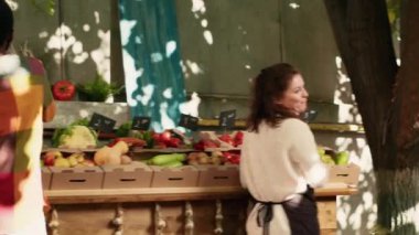 Sadık müşterileri kucaklayan ve selamlayan mutlu kadın satıcı, gıda pazarında pozitif hissediyor. Çiftçi pazarında sarılan genç kadınlar, düzenli müşterilerin ziyaretinden keyif alıyorlar. El kamerasıyla..