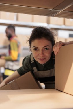 Karton kutularla çalışan gülen bir çalışan depoda müşteri paketleri hazırlıyor. Depo amiri ambalajları paketliyor ve depoda teslimat işlemlerini yönetiyor.