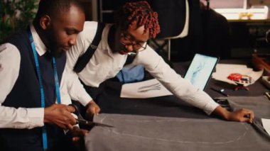 İki modacı atölyede modern giyim ürünleri için malzeme kesiyor, el yapımı atölye işlemleri için kumaş üzerinde makas kullanıyorlar. Tasarımcılar takımı terzilik ve nakış işine hazırlanıyor..