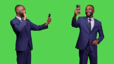 Şirket çalışanı, yeşil ekran geçmişi üzerinden iş videosu toplantısına katılıyor, uzaktan video konferans görüşmesinde insanlarla konuşuyor. Çevrimiçi telekonferans ve cep telefonu kullanan erkek model.