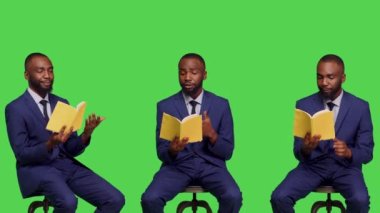 Modern girişimci stüdyoda edebiyat kitabı okuyor, ofis elbisesi giyiyor ve sandalyede oturuyor. Olumlu iyimser adam, yeşil perde arkaplanı üzerine ders veriyor..
