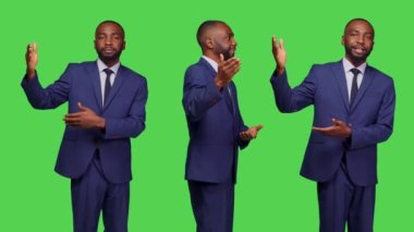 Stüdyoda reklam sunumu yapan profesyonel bir çalışan yeşil ekran arkaplanının soluna ya da sağına işaret ediyor. Reklam yaratmak için ofis kıyafeti giyen bir erkek ofis çalışanı..