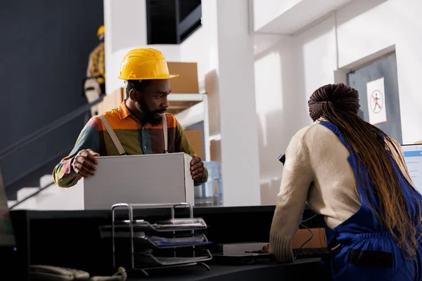 发货经理在接待处等包裹电子发票 非洲裔美国仓库工人戴着安全帽 在收银台上放有客户订单的纸盒 — 图库照片