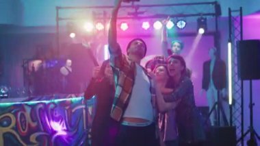 Çeşitli yetişkinler dans pistinde renkli ışıklar altında fotoğraf çekiyorlar ve parti kutlamalarında eğleniyorlar. Neşeli erkekler ve kadınlar disko etkinliği videolarının keyfini çıkarıyorlar. El kamerasıyla..