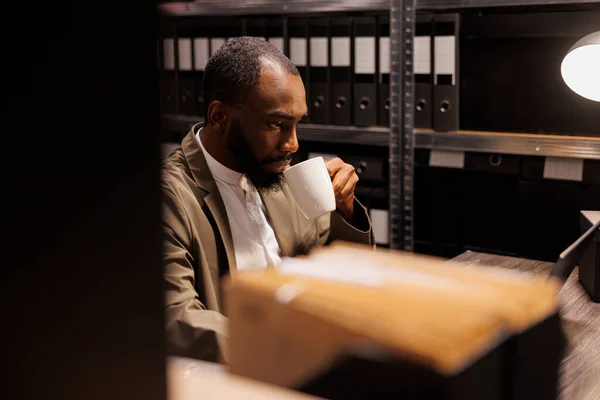 非裔美国警察喝咖啡 用笔记本电脑分析线索 刑侦人员检索警察档案中的信息 研究计算机上的犯罪案件证据 — 图库照片