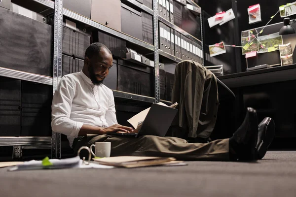 非洲裔美国调查人员 坐在黑暗的办公室地板上 用笔记本电脑分析犯罪案件 侦缉员检查警方报告及进行调查 — 图库照片