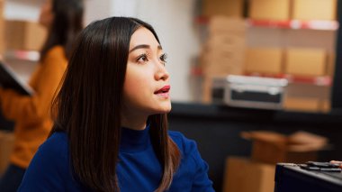 Dizüstü bilgisayardaki üretim notlarına bakan, iş yönetimi planlayan ve hisse senedi lojistiği kullanan bir kadın. Depoda paketlerle girişimci olarak çalışan genç bir yetişkin. El kamerasıyla..