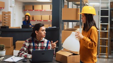 Asian woman presenting warehouse products to man, people working on merchandise quality control in storage room. Young employees looking at goods in boxes, small business plan.