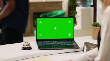 Otel personeli laptopta yeşil ekran kullanıyor. Resepsiyonda insanlara yardım ediyor. Boş model şablonu, tropikal deniz kenarı tatil beldesi ile izole edilmiş ekrana bakan resepsiyonist.