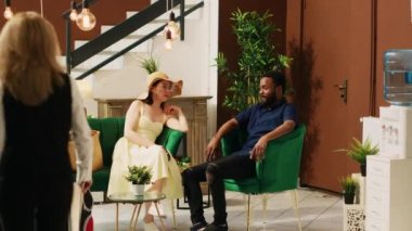 Otel çalışanları lobide misafirlerle konuşuyor, dinlenme odasında bekleyen insanlara lüks hizmetler sunuyorlar. Çalışanlar oda rezervasyonu olan çiftlere tropikal aktiviteler öneriyor..