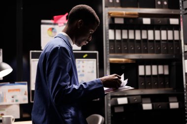 Muhasebeci bürokrasi kayıtlarını okuyor, şirket deposunda muhasebe raporunda çalışıyor. Resmi takım elbiseli Afrikalı Amerikalı işadamı depodaki yönetim dosyalarını analiz ediyor.
