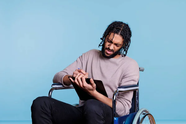 Zdezorientowany Arabski Mężczyzna Wózku Inwalidzkim Trzymający Długopis Schowek Podczas Wypełniania — Zdjęcie stockowe