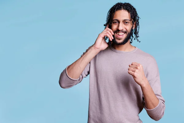 快乐的Arab男人在智能手机上说话 用紧握着的手像表现出胜利的姿态 兴高采烈的人一边接电话 一边看着摄像机听好消息 — 图库照片