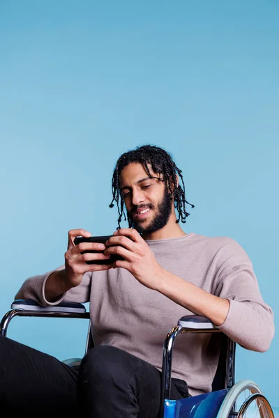 坐在轮椅上的快乐的Arab游戏玩家 一边玩着手机 一边开心地满脸笑容 笑着让身体残疾的男人享受智能手机上的在线游戏应用 — 图库照片