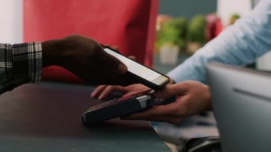 Moda mağazasının masasında şık kıyafetler alan şık bir adam cep telefonuyla ödeme yapıyor. Modern butikte resmi kıyafetler için Afrika kökenli Amerikalı müşteri alışverişi. Moda konsepti