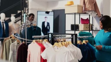 Shooper Asyalı işçilerden moda gömlekler için yardım istedi, modern butikte malzeme konusunu tartıştı. Afro-amerikan müşteri giyim mağazasından şık kıyafetler alıyor.