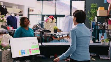 Kafkasyalı yönetici modern butikte mağaza tarayıcısı kullanarak müşteri kıyafetlerini tarıyor. Afro-Amerikalı bir kadın alışveriş merkezinden şık ürünler alıyor, yeni kıyafetler istiyor. Moda konsepti