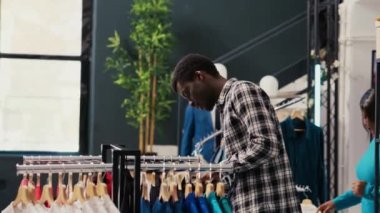 Afro-Amerikalı alışverişçi şık gömlekleri analiz ediyor, almadan önce elbise kumaşlarını kontrol ediyor. Giyim mağazasından şık ürünler ve aksesuarlar almak için alışveriş kolik müşteri alışverişi