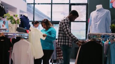 Afrika kökenli Amerikalı çift şık ürünleri kontrol ediyor, modern butikte günlük kıyafet alışverişi yapıyorlar. Moda müşterileri giyim mağazasında moda kıyafet malzemelerini inceliyor. Moda konsepti