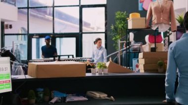 Afro-Amerikan kurye mağaza müdürüne dağıtım raporunu gösteriyor, müşterilerin modern butikte detaylarını tartışıyor. Çalışan alışveriş merkezinde teslimat için paketler hazırlıyor
