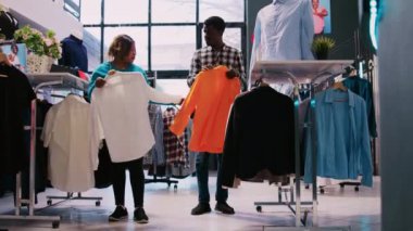 Afro-amerikan müşteriler indirimli ürünlere bakıyor, modern butikte resmi giysiler alıyorlar. Moda bir çift alışveriş merkezinde şık kıyafet malzemelerini kontrol ediyor. Moda konsepti