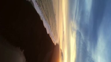 Dikey video: İzlanda siyah kumlu plaj havadan görüntüsü, kıyı şeridine dalgaların çarptığı muhteşem Atlantik kıyısı. Kutup manzarası, karlı dağlar ve kumsaldaki siyah kumlar, soğuk manzaralar. 60