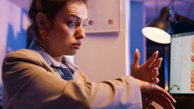 Executive manager checking wristwatch in office, looking at time and working overhours on corporate development. Female worker analyzing financial diagrams on screen, profit growth. Handheld shot.