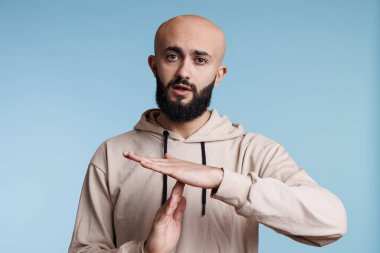 Arap adam kameraya bakarken elleriyle jest yapıyor. Genç, kel, sakallı, konuşmayı durduran, silah stüdyosunun portresiyle kesme sinyali veren kişi.