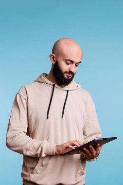 Genç Arap adam dijital tablette uygulama kullanıyor, dokunmatik ekranda mesaj yazıyor. Odaklanmış kişi taşınabilir aygıt tutuyor, İnternet sayfalarına bakıyor ve sosyal medyada geziniyor