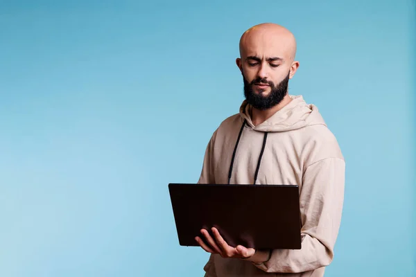 ラップトップを持つ若いアラブ人男性に焦点を当て ソフトウェアアプリを開発しながらコードを分析する 携帯型コンピュータ上でアプリケーションを使用している間 困惑式思考を持つ混乱した人 — ストック写真